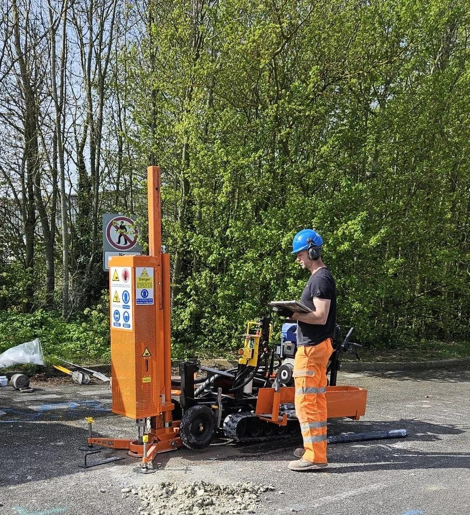 Operator reviewing field data on a tablet next to the drilling rig in a green wooded setting.